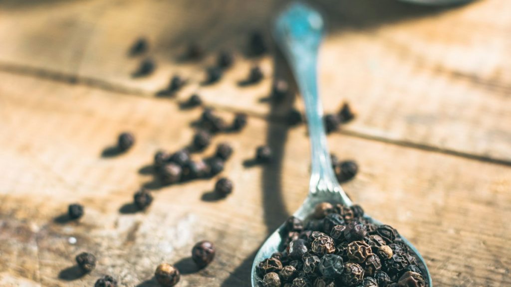 Black peppercorns on a spoon, showing berry size and density
